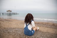 一名女子穿着休闲装，坐在安塔利亚的沙滩上，俯瞰着大海和木制码头