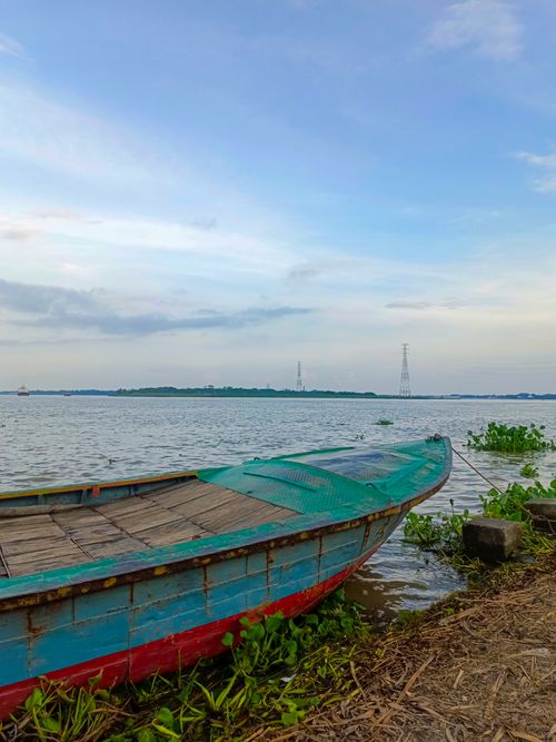 Free Peaceful scene of a colorful wooden boat docked by the calm water under a blue sky. Stock Photo