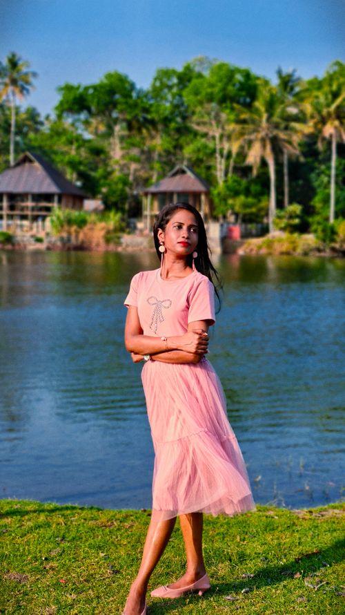 Free Woman in pastel pink by a tranquil lake, embodying a serene summer getaway. Stock Photo