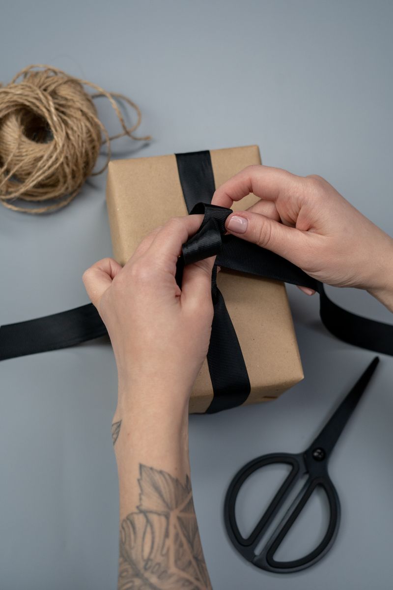 Close-up of hands tying a black ribbon around a gift box