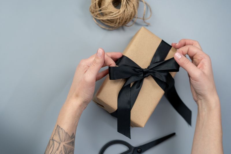Close-up of hands wrapping a gift box with a black ribbon