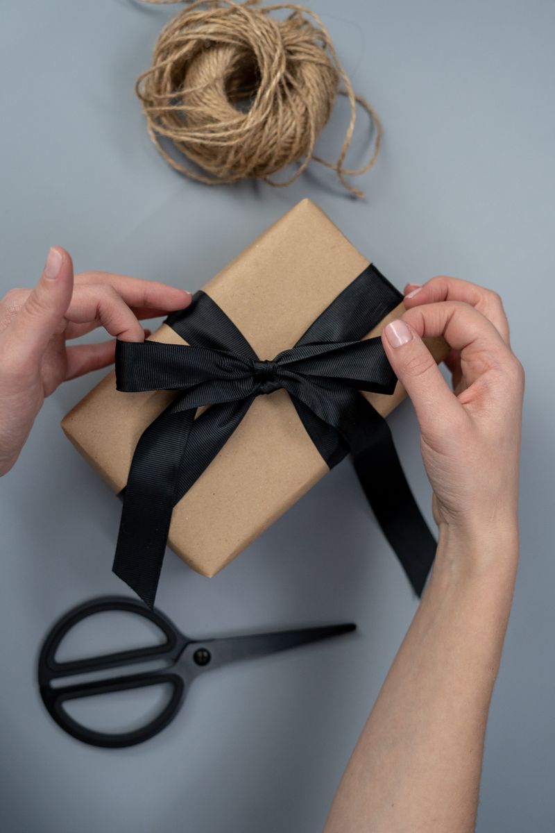 Hands tying a black ribbon on a craft paper gift box