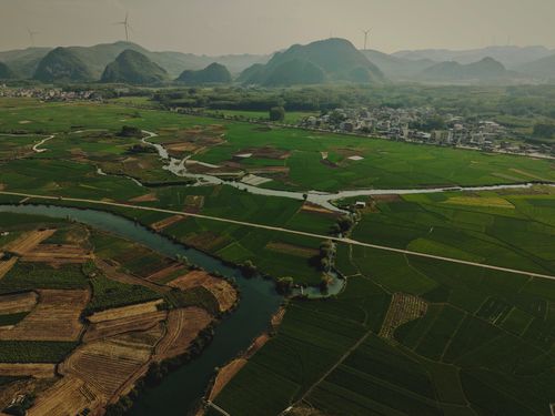 Free A scenic aerial shot capturing lush green farmlands, mountains, and wind turbines under a clear sky. Stock Photo