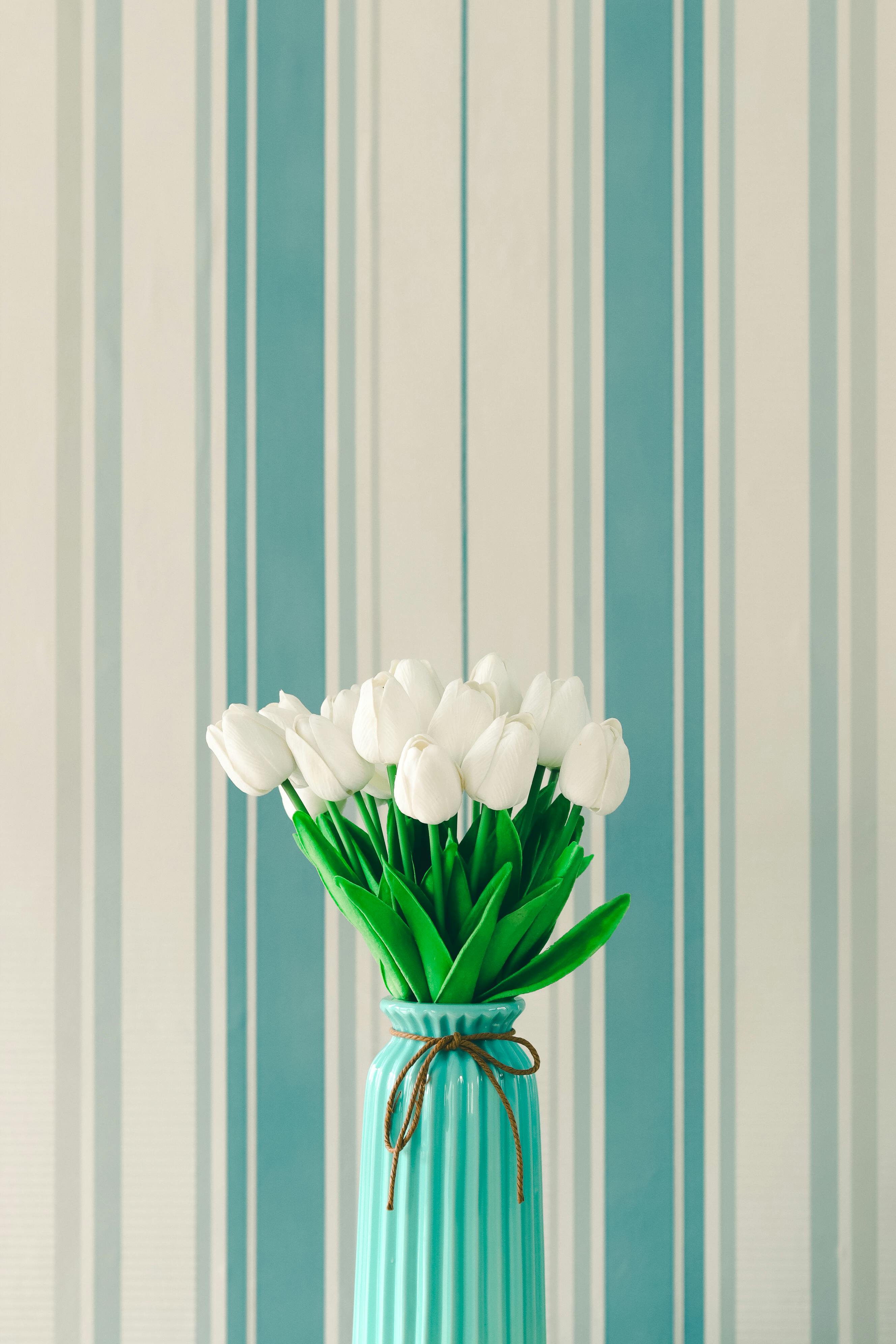A minimalist floral arrangement of white tulips in a turquoise vase with a striped background, perfect for interior design inspiration.