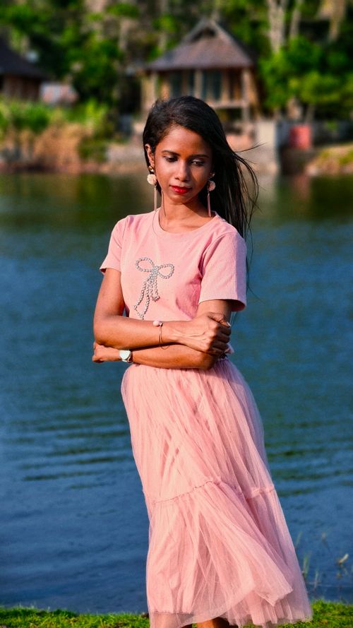 Free A serene portrait of a woman in a pastel pink dress posing by a calm lakeside. Stock Photo
