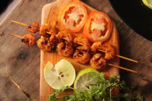 Free Delicious grilled shrimp skewers served with lime and tomato slices on a wooden board. Stock Photo