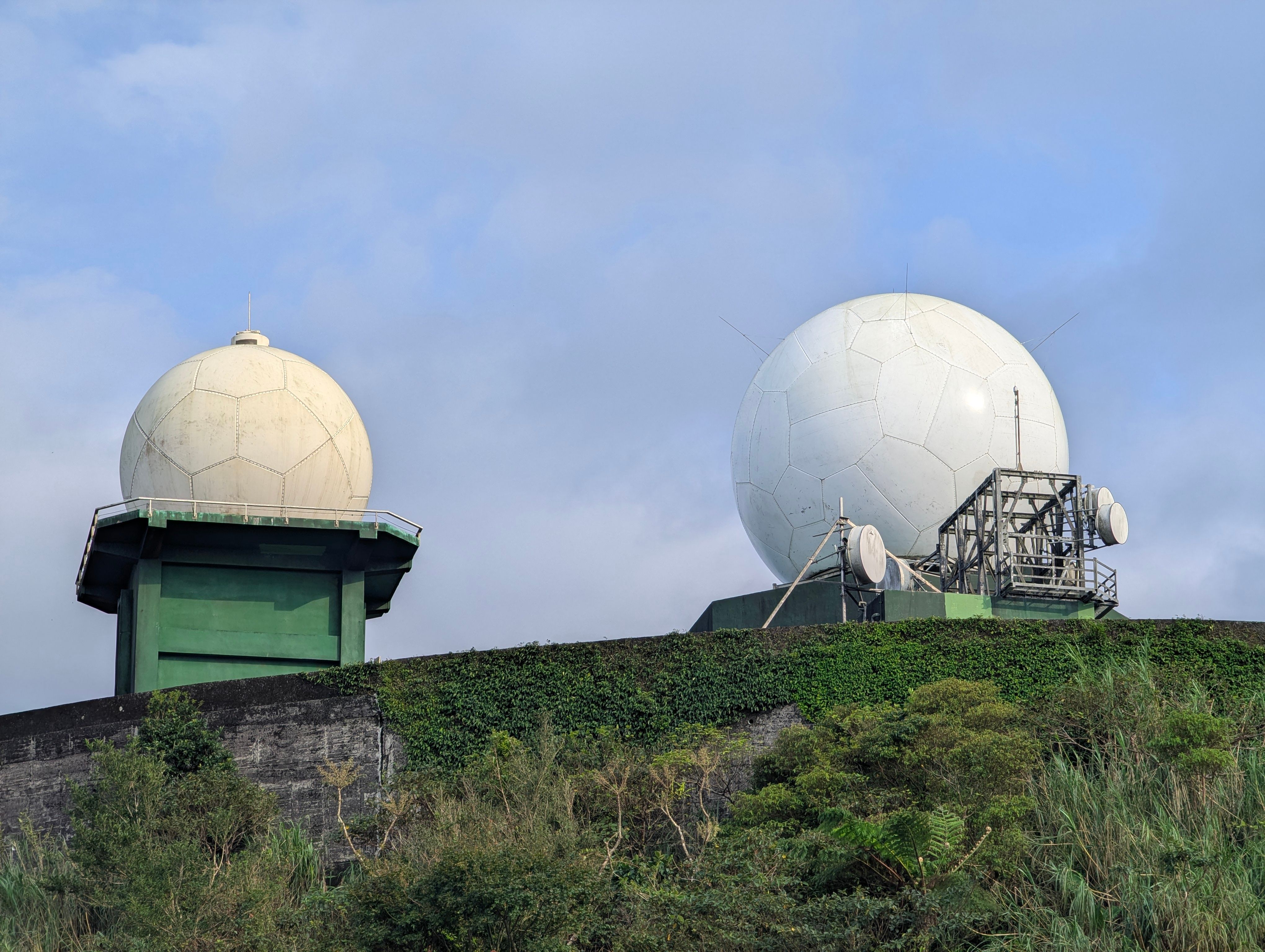 Radar domes on a lush hill in New Taipei City, Taiwan, contrasting technology with nature.