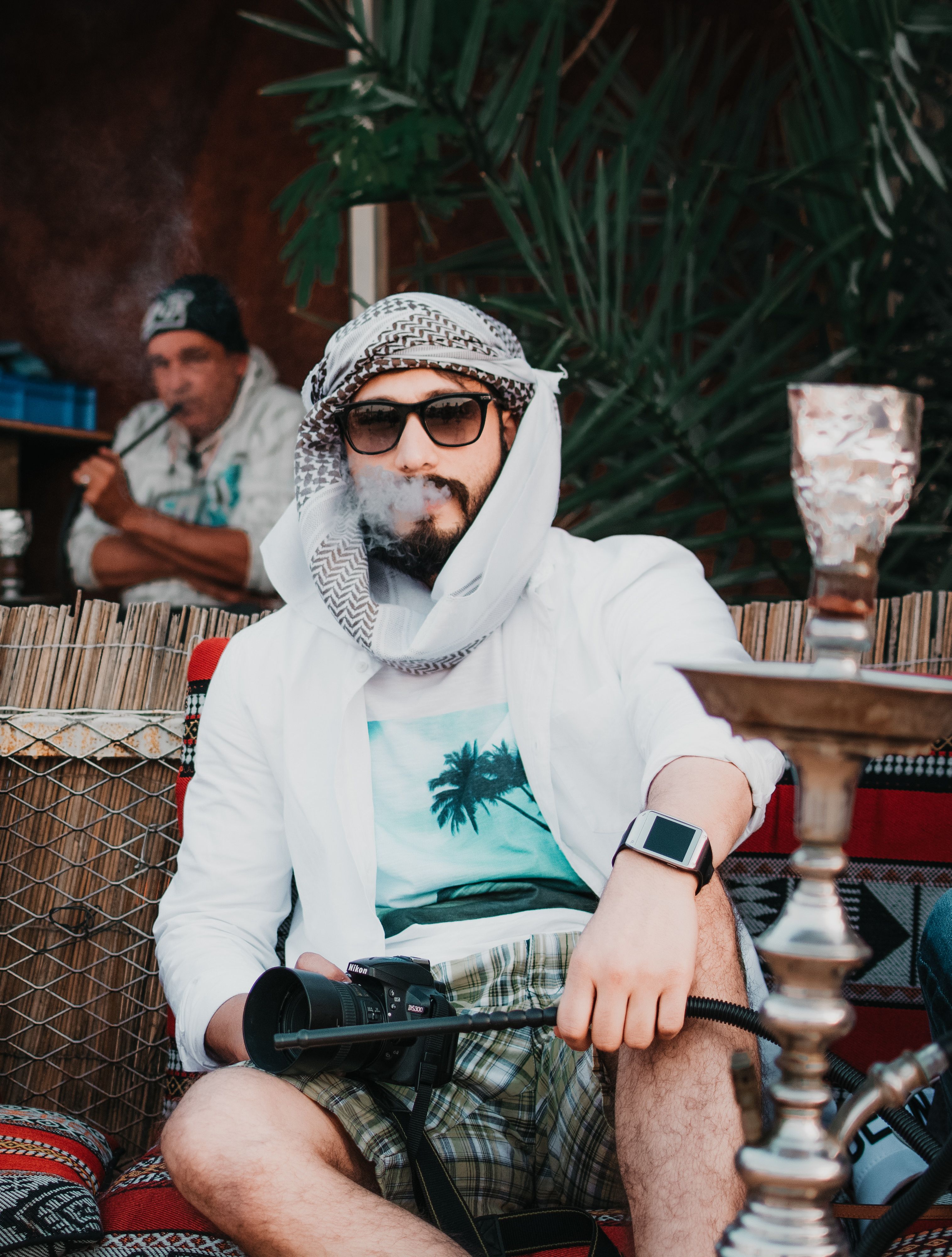 Man wearing sunglasses and headscarf smoking shisha outdoors, with a relaxed vibe.