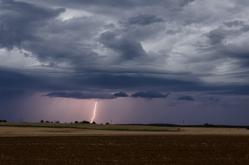 Free Striking lightning bolt under dark storm clouds over rural fields in France. Stock Photo