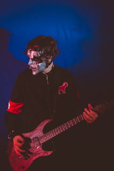 A masked guitarist passionately plays rock music on stage under dramatic lighting.
