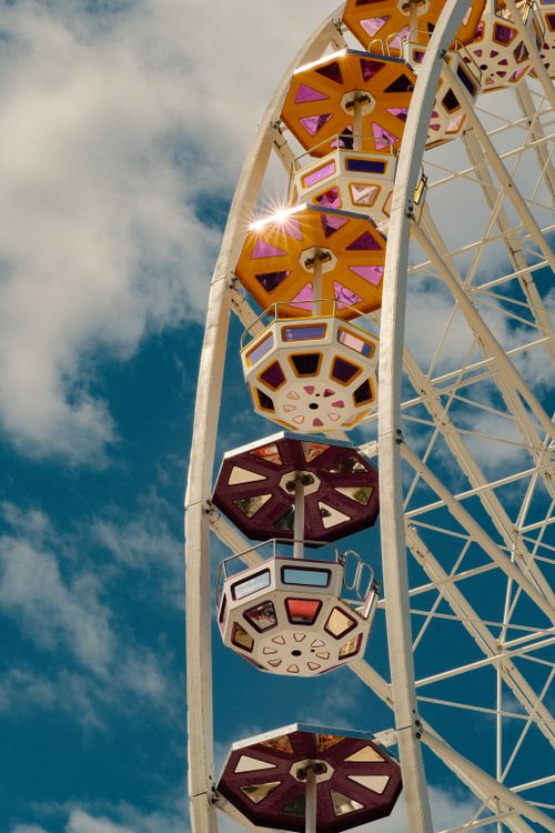 Free Vibrant Ferris wheel gondolas with sun flare and clouds in the background. Stock Photo