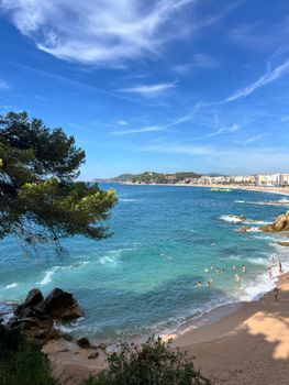 Scenic view of a sandy beach and clear blue waters on Costa Brava, Spain, under a bright sky.