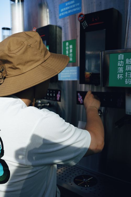 Free A person wearing a hat uses an automated drink dispenser on a sunny day. Stock Photo