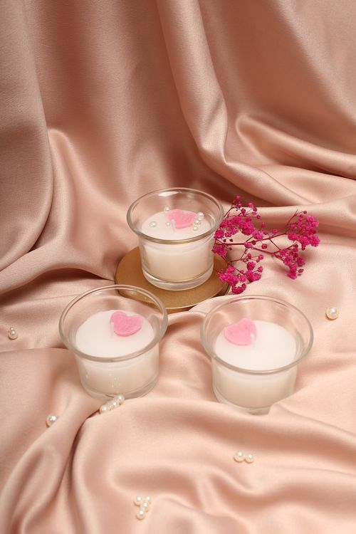 Free A set of three elegant candles with pink decorations on satin fabric, creating a romantic ambiance. Stock Photo