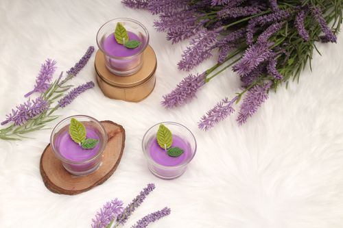 Free Lavender scented candles on a wooden base surrounded by artificial lavender flowers on a fluffy background. Stock Photo