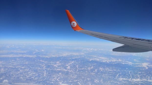 Stunning aerial view of an airplane wing from high altitude, flying over snowy mountain range on a clear day.