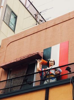 A colorful samurai statue decorates an urban balcony beneath rooftop antennas and buildings.