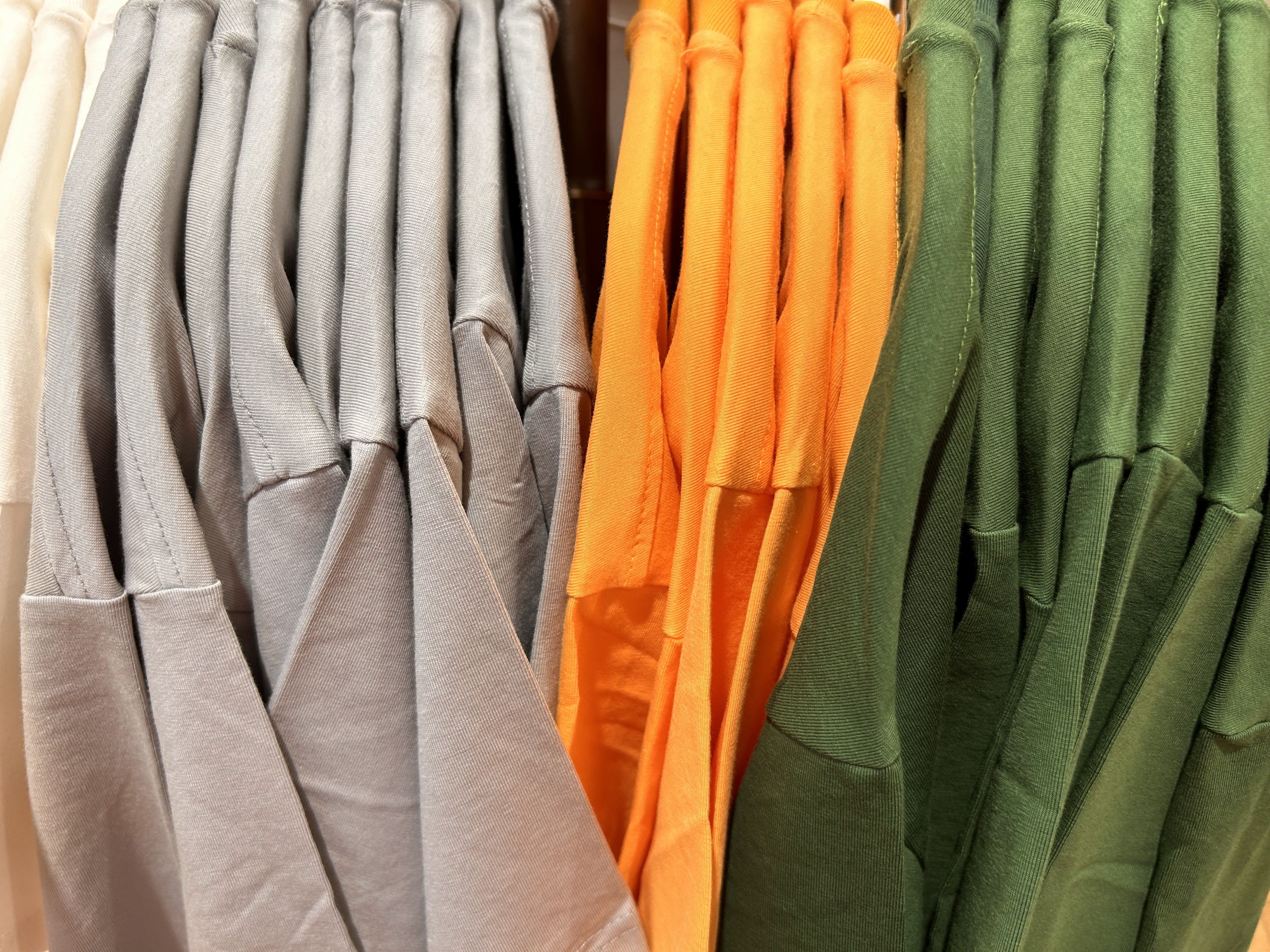 Neatly arranged t-shirts in gray, orange, and green on store rack
