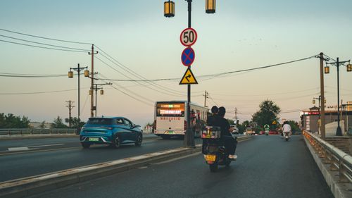 Free Street view of urban traffic with motorbikes and cars during sunset on a bridge, highlighting road signs. Stock Photo