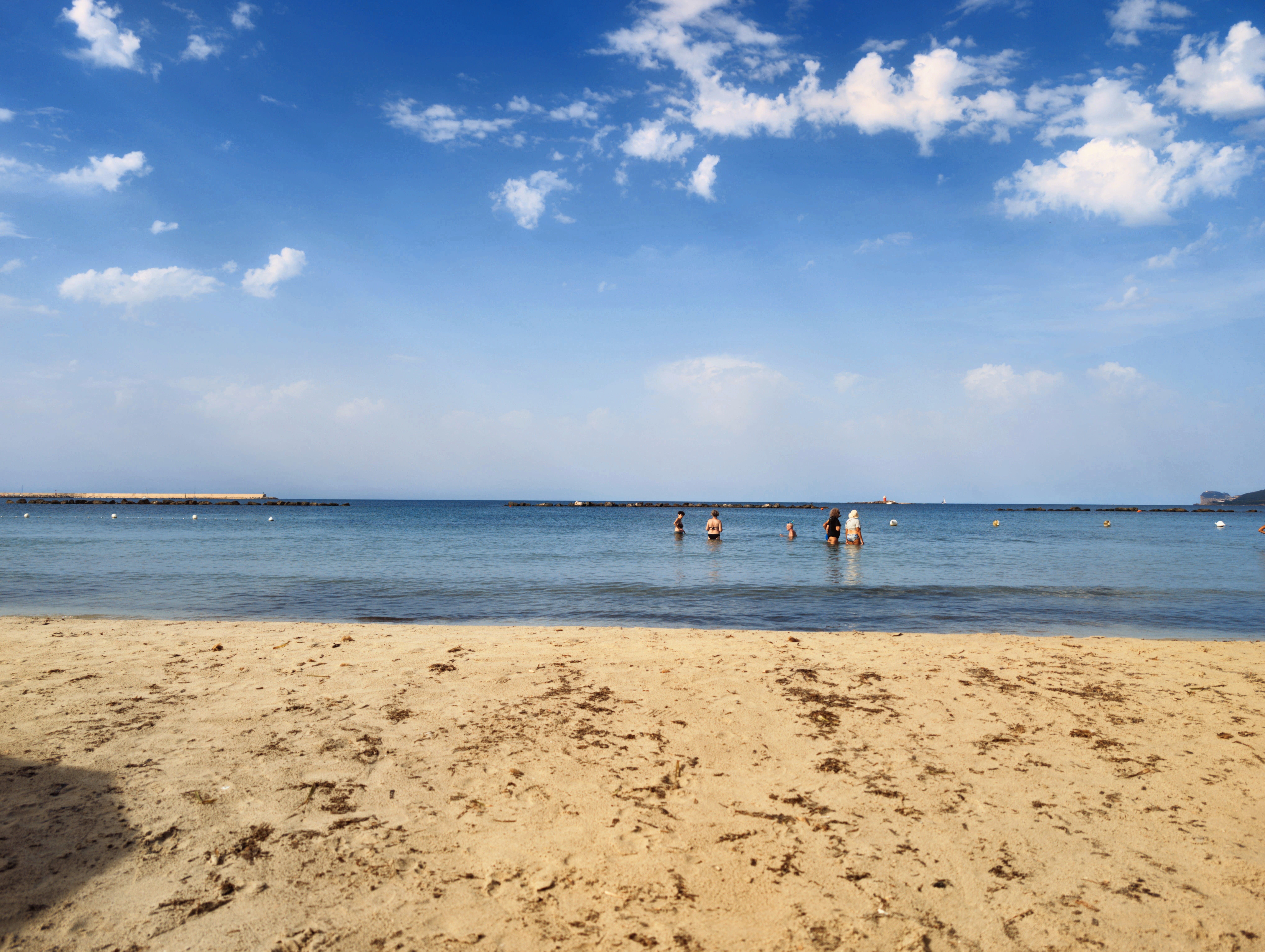 Relaxing beach scene with people enjoying the calm sea under a bright blue sky.