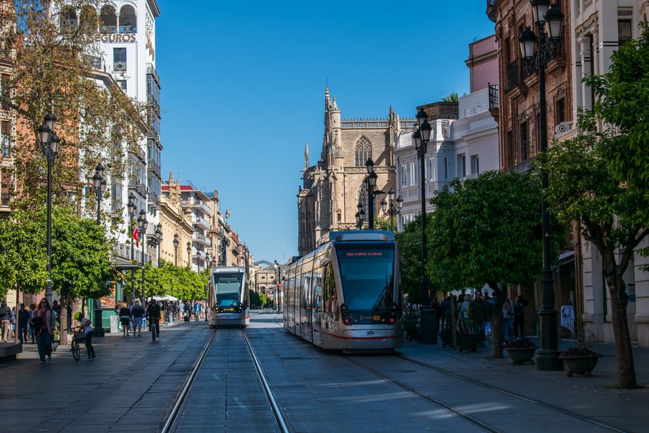 Los tranvías recorren la Avenida de la Constitución en Sevilla, mostrando la arquitectura urbana y la vida callejera.
