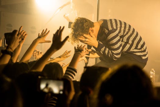 Energetic male musician in striped sweater engages with enthusiastic concert crowd.