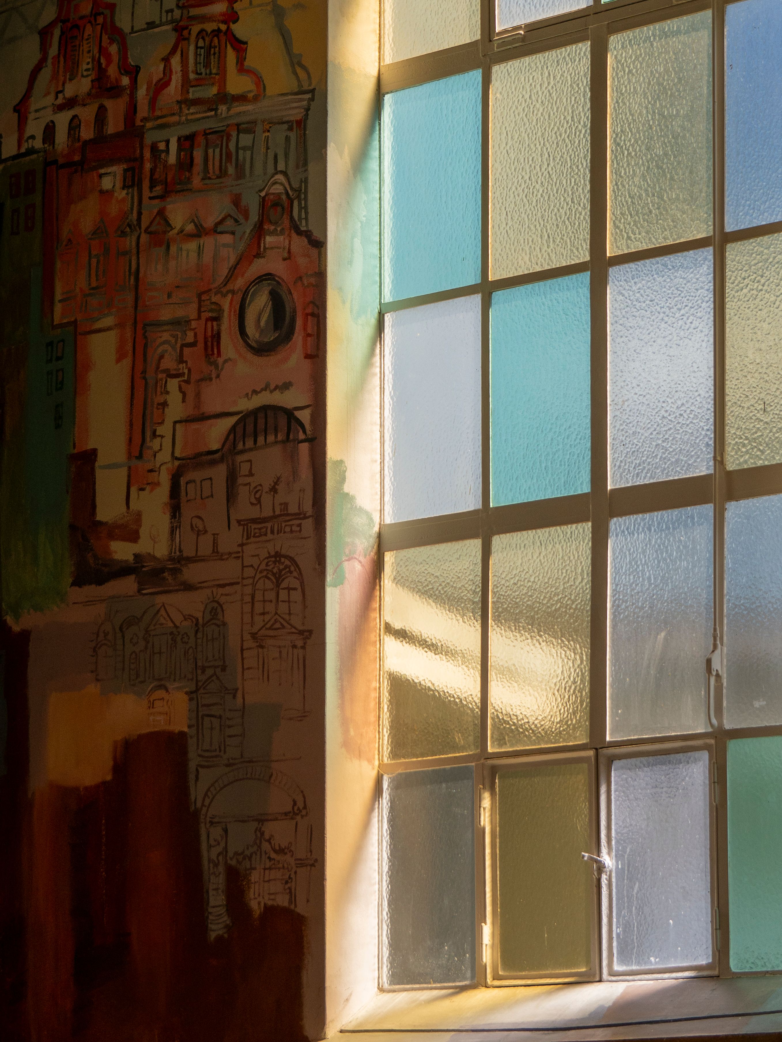 Warm sunlight through a stained glass window illuminates an artistically painted wall.