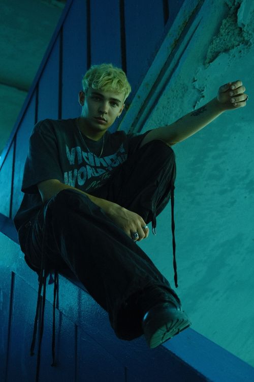 Free Young man with blonde hair sitting in a moody urban setting, deep in thought. Stock Photo