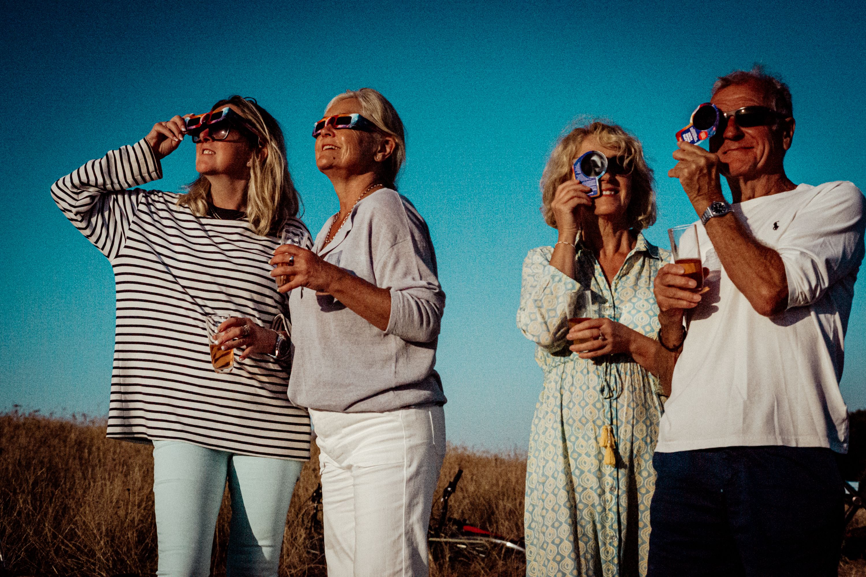 Group of adults watching a partial solar eclipse with protective glasses on a sunny day.