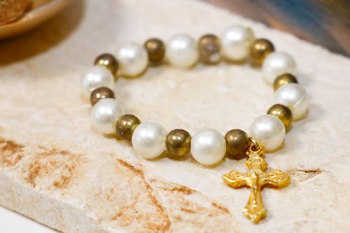 Free Close-up of a pearl bracelet featuring a gold cross pendant on a textured surface. Stock Photo