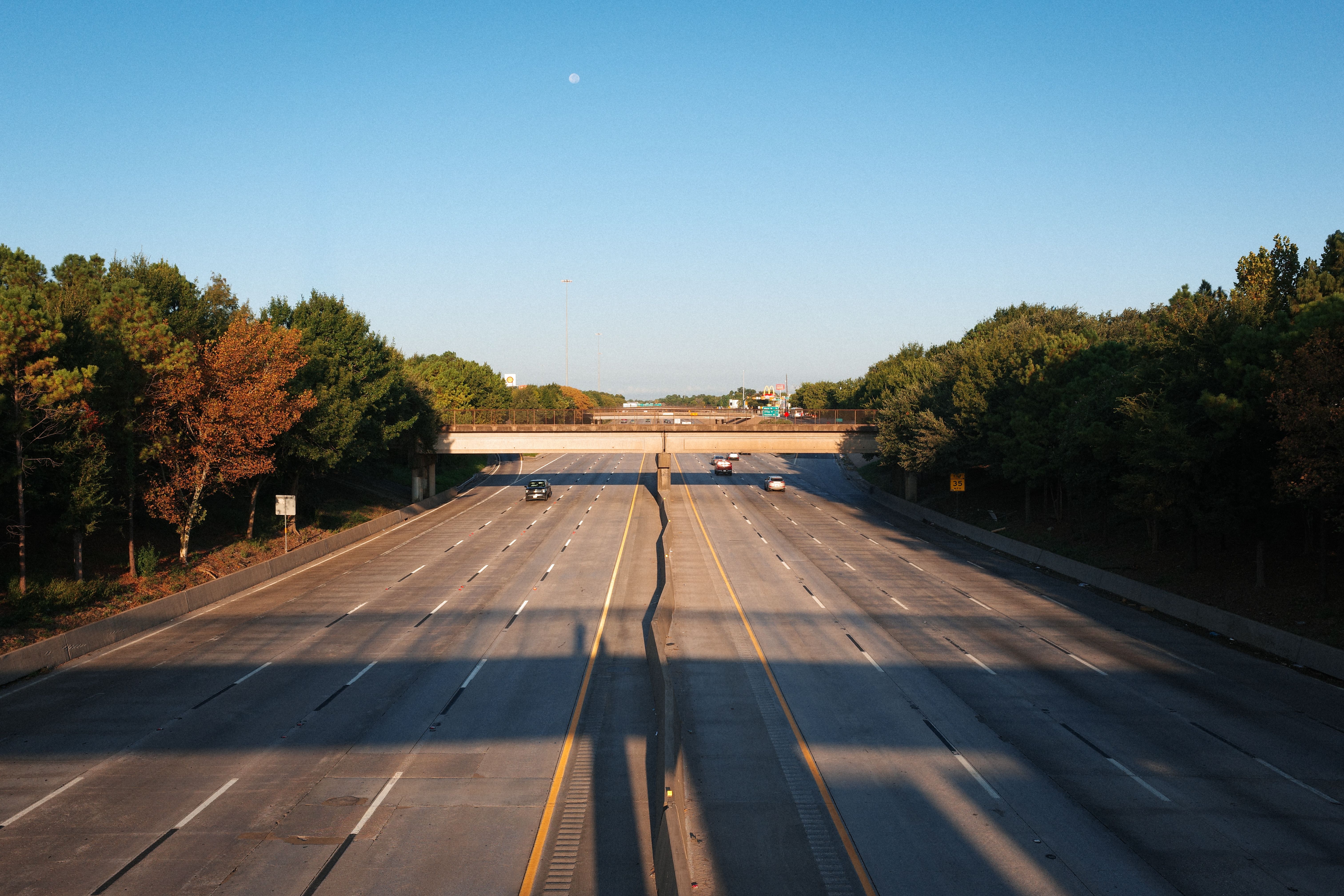An empty highway in Houston, Texas, featuring autumn-colored trees and a clear sky.