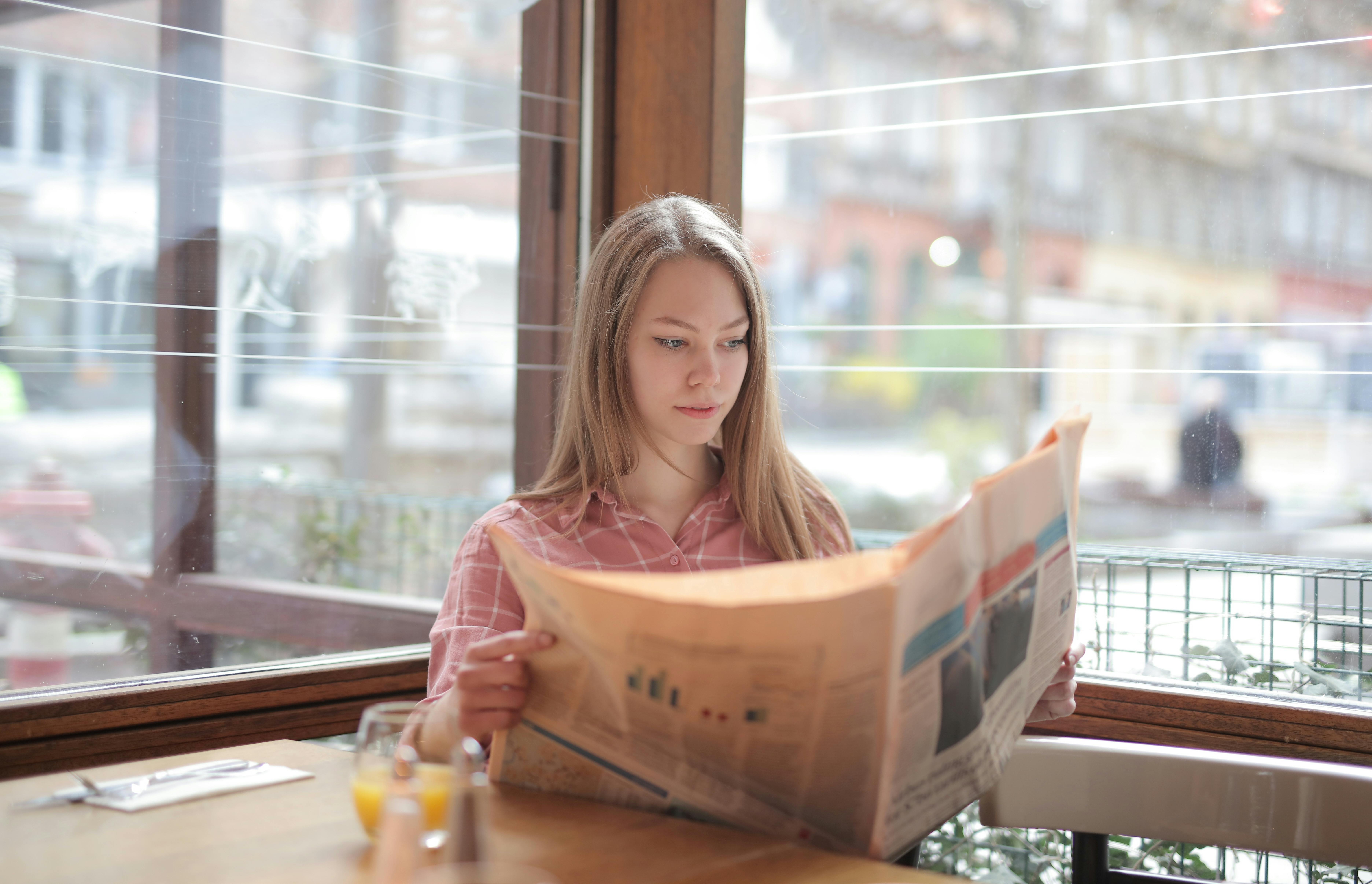woman in pink long sleeve shirt reading the newspaper