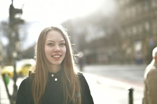 Free A young woman smiling brightly outdoors on a sunny street. Stock Photo