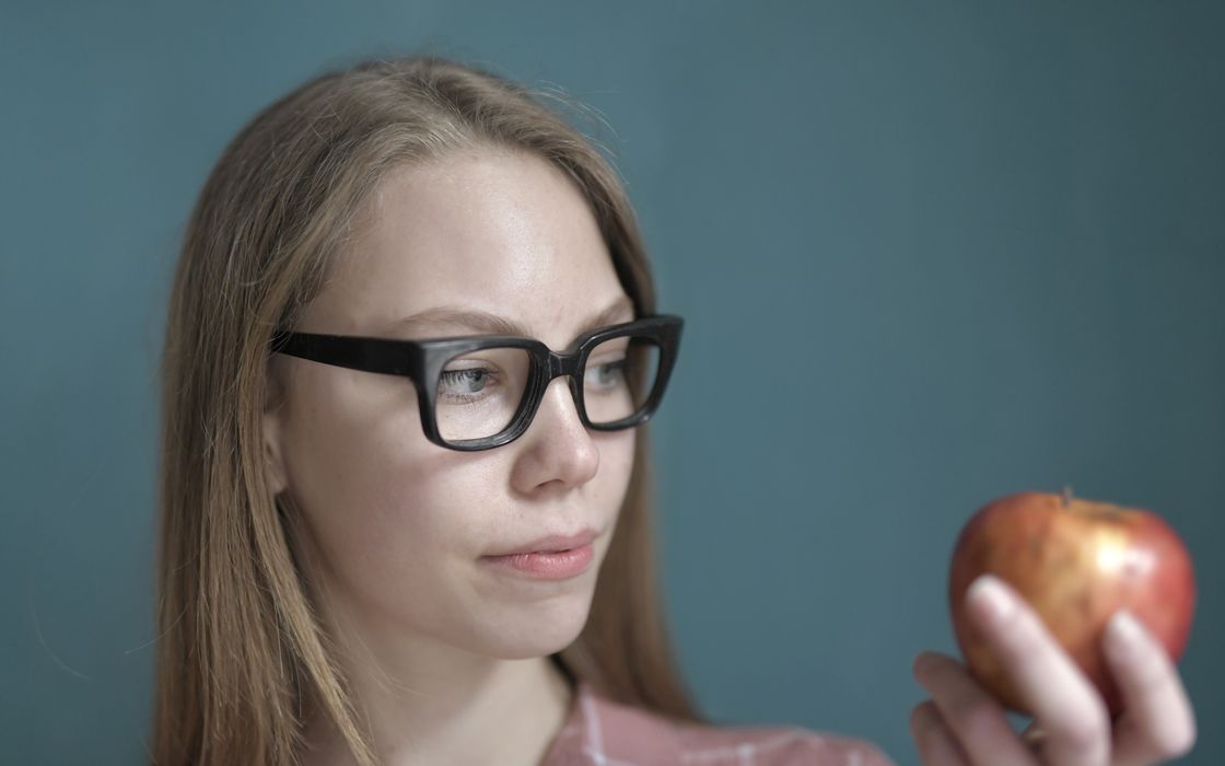 Woman in glasses looking thoughtfully at an apple while weighing up a health decision