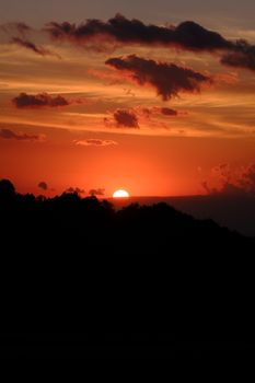 Dramatic red sunset with clouds over silhouetted hills, creating a breathtaking scene.