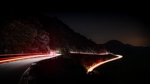 Free A serene night scene featuring car light trails on a curvy road through mountains. Stock Photo