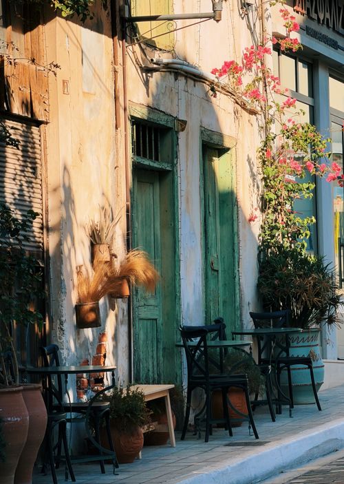 Free A cozy cafe setting in Crete featuring weathered green doors, floral decorations, and outdoor seating bathed in warm sunlight. Stock Photo