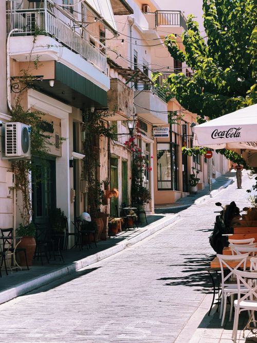 Free Picturesque street in Agios Nikolaos, Crete, Greece with outdoor cafes, shops, and vibrant greenery. Stock Photo