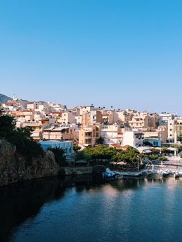Scenic view of Agios Nikolaos harbor with vibrant buildings under a clear blue sky in Crete, Greece.