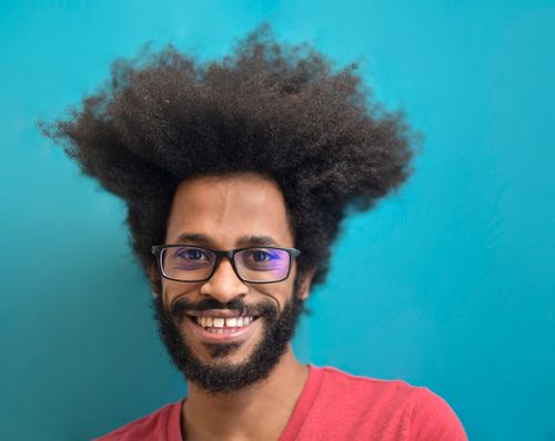 Free Vibrant portrait of a smiling man with afro hair and glasses against a teal background. Stock Photo