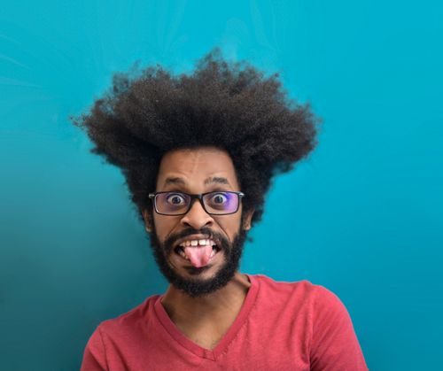 Free A humorous portrait of a man with an afro making a silly face against a turquoise background. Stock Photo