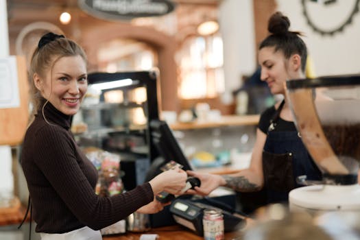 A smiling customer makes a contactless payment at a bustling café counter.