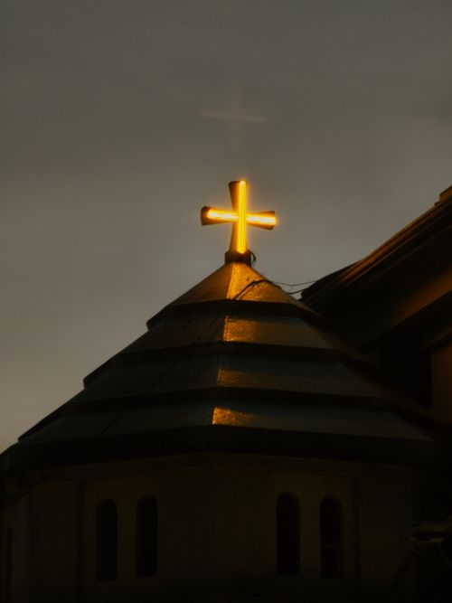 Free Golden cross atop a church roof glowing against an evening sky, symbolizing faith. Stock Photo