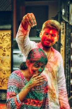 Positive man spilling colorful powder on laughing Indian woman while having fun during Holi festival on town street