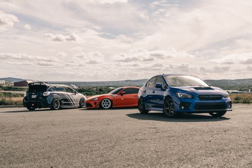 Free Three vibrant sports cars parked on an open road under a partly cloudy sky, showcasing modern automotive design. Stock Photo