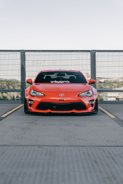 Free Front view of a bright orange sports car in an empty parking lot, showcasing sleek design. Stock Photo