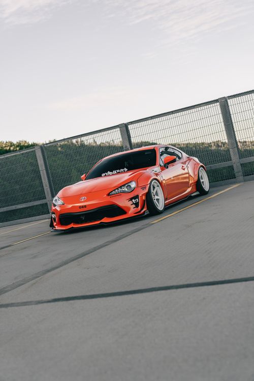 Free A vibrant red sports car with custom mods parked in an industrial area, showcasing urban automotive style. Stock Photo