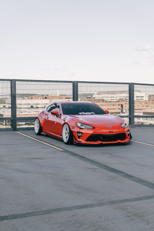 Free A vibrant red sports car parked on an urban rooftop with a city backdrop, capturing modern automotive design. Stock Photo