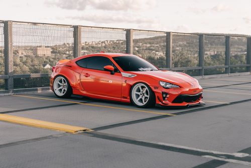 Free Stunning bright orange sports car parked in an urban rooftop setting on a sunny day. Stock Photo