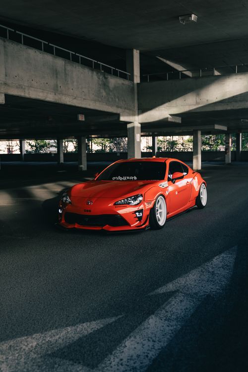 Free Sleek red sports car parked in a shadowy urban garage, highlighting its modern design. Stock Photo